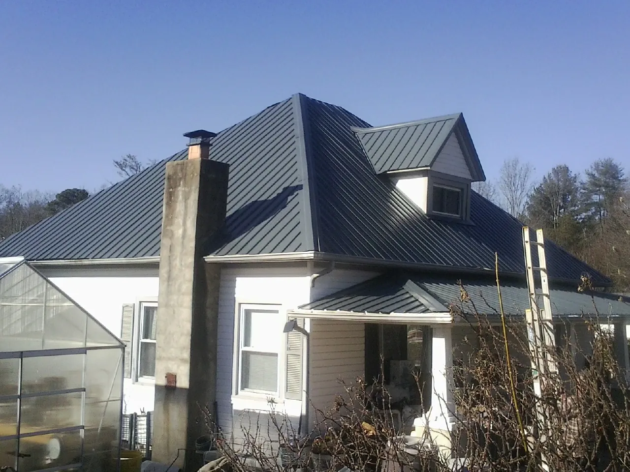 Dark blue standing seam metal roof on a white farmhouse with dormer — Slate & Tile Roof Repair by Roofing Brothers in Quaker Hill