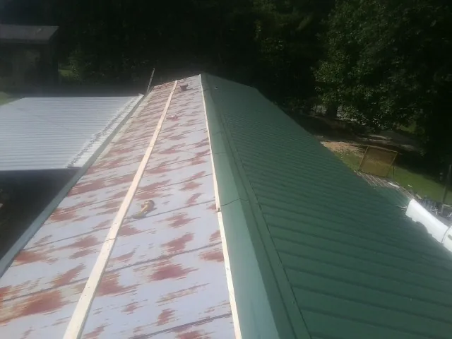 Old rusted panels beside newly installed green metal roofing — Wind Damage Roof Repair by Roofing Brothers in Quaker Hill