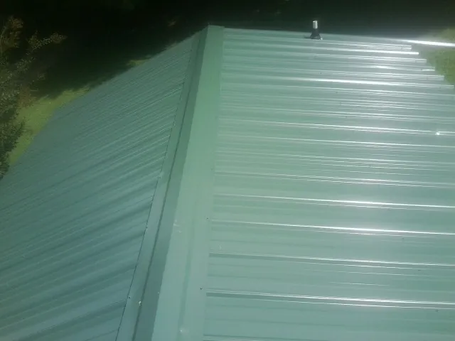 New green metal panels meeting at the ridge of a roof — Flat Roof Repair work by our crew in Quaker Hill