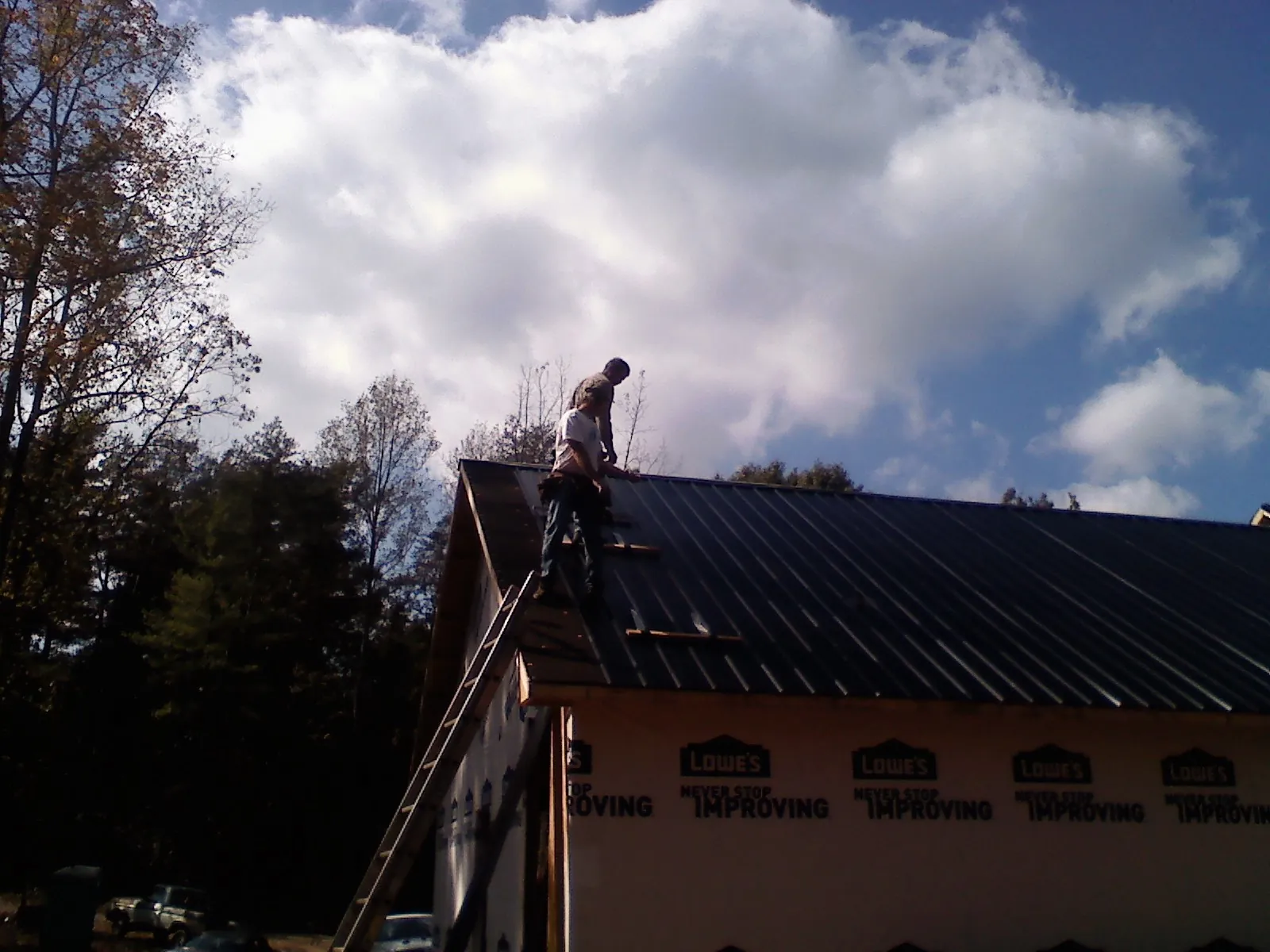 Roofer fastening dark metal panels high against a cloudy sky, from a Roof Inspection job in Quaker Hill