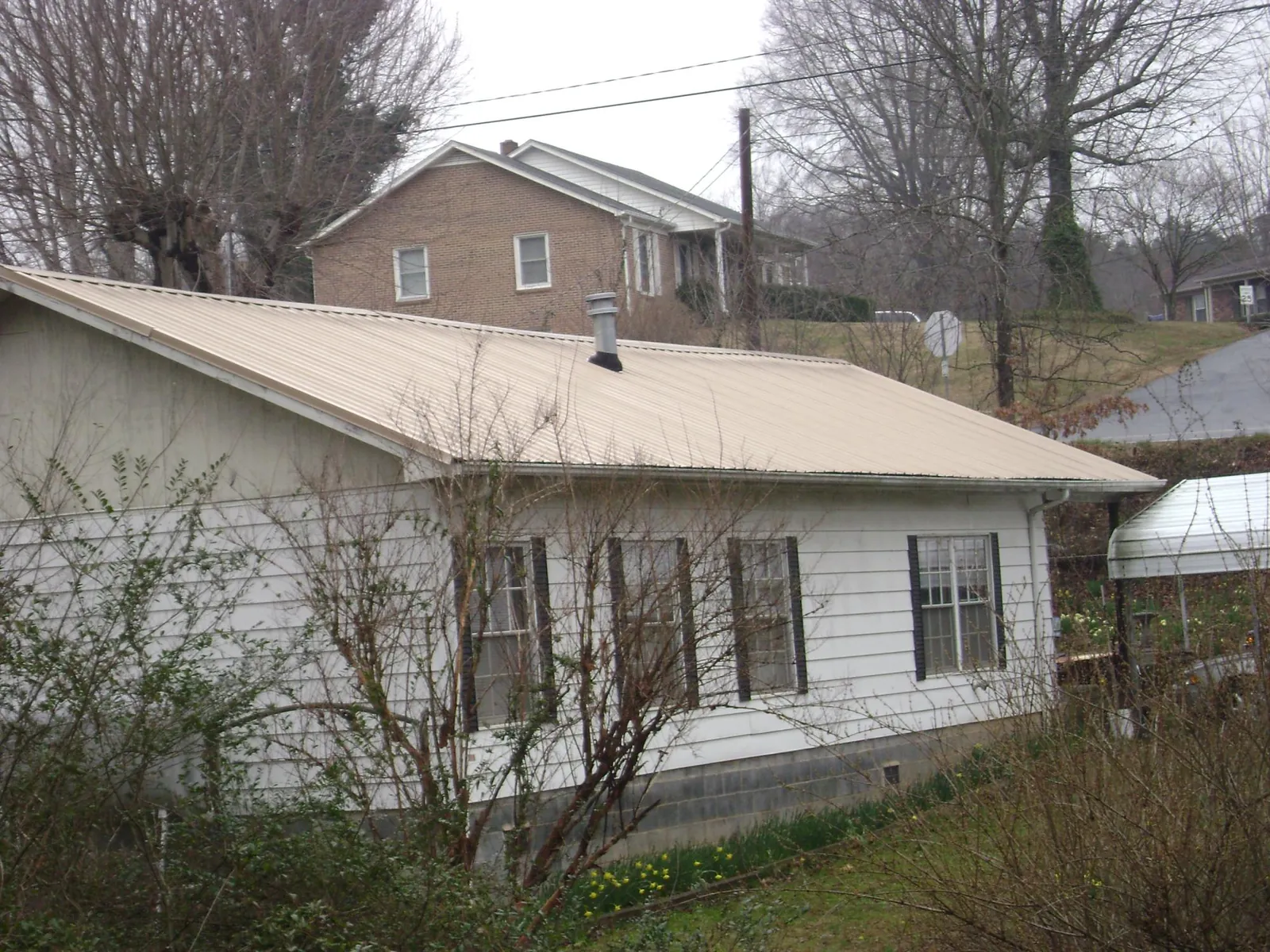 Tan metal roof on a white sided house set into a hillside — Commercial Roofing by Roofing Brothers in Quaker Hill