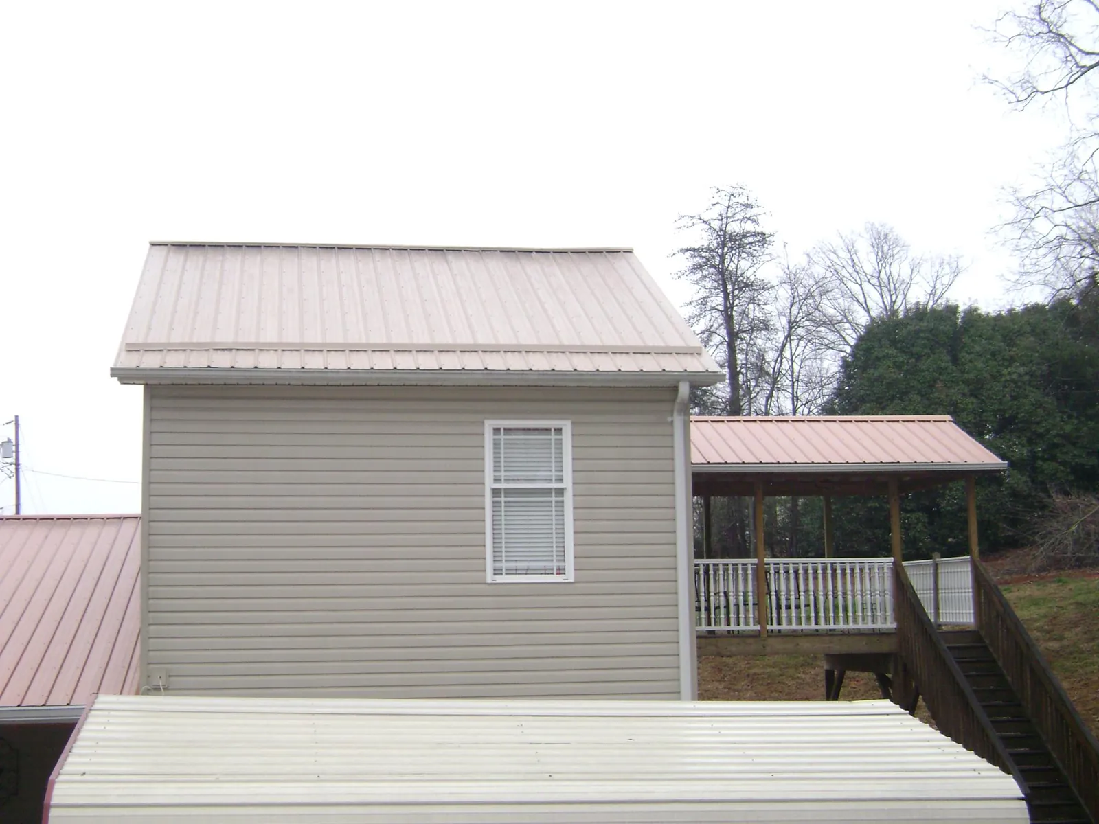 Tan metal roofs on a two story addition and attached porch, from a Roof Replacement job in Quaker Hill
